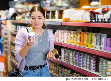 Young cheerful woman buying canned pet food in pet store Young cheerful woman buying canned pet food in pet store 136400073