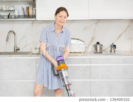 Housewife using vacuum cleaner removes dust in room Housewife using vacuum cleaner removes dust in room 136400102