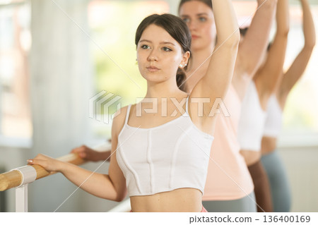 Fit happy young girls practice at ballet standing in fourth position at barre in choreography studio Fit happy young girls practice at ballet standing in fourth position at barre in choreography studio 136400169