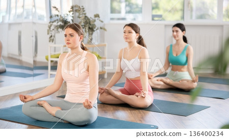 Meditation in lotus position during yoga class in studio. Women meditating Meditation in lotus position during yoga class in studio. Women meditating 136400234