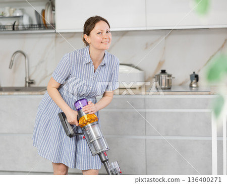 Housewife using vacuum cleaner removes dust in room Housewife using vacuum cleaner removes dust in room 136400271