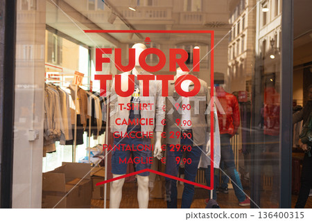 Clothing store window with sale sign in Rome. A clothing store window displays a red sale sign with prices written in Italian Clothing store window with sale sign in Rome. A clothing store window displays a red sale sign with prices written in Italian 136400315