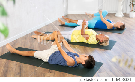 Mom, grandmother and teen grandson do preparatory stretching, lying on back and benting leg at knee 136400321