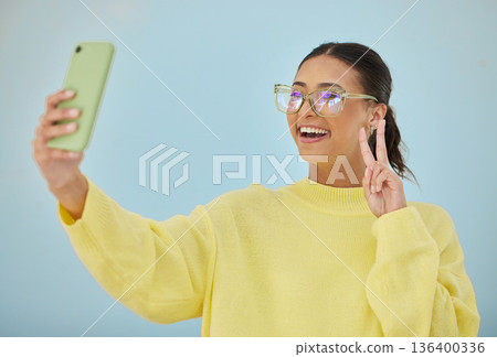 Selfie, peace sign and happy studio woman with emoji v sign, icon and pose for social network, memory picture or photography. Gen z person, youth or influencer post to media app on blue background Selfie, peace sign and happy studio woman with emoji v sign, icon and pose for social network, memory picture or photography. Gen z person, youth or influencer post to media app on blue background 136400336