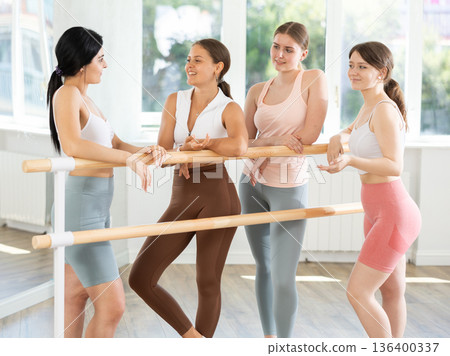 Young ballerinas chatting joyfully standing around training barre Young ballerinas chatting joyfully standing around training barre 136400337