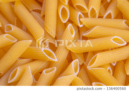 Uncooked penne with rustic ambiance, Uncooked penne scattered in rustic kitchen setting, Raw penne pasta arranged in rustic kitchen scene highlighting homemade cooking themes 136400560