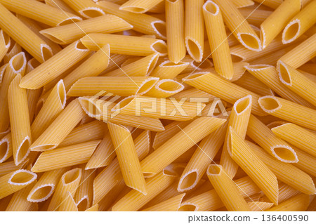 Smooth textured penne pasta background suitable for advertising purposes, Detailed image of ridged penne pasta featuring warm hues and tactile surface for marketing use Smooth textured penne pasta background suitable for advertising purposes, Detailed image of ridged penne pasta featuring warm hues and tactile surface for marketing use 136400590