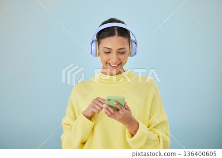 Woman with phone, headphones and mockup in studio for social media post, mobile app and streaming radio site. Smile, music media subscription and happy girl with cellphone on blue background space. Woman with phone, headphones and mockup in studio for social media post, mobile app and streaming radio site. Smile, music media subscription and happy girl with cellphone on blue background space. 136400605