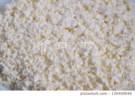 Closeup curd cheese mass showing crumbly white clusters, artisan cheesemaker inspection implied, rustic farmhouse mood, soft natural light highlighting texture and milk fat 136400646