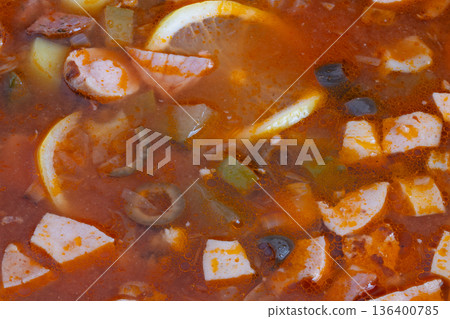 Hearty solyanka simmering on stove with chunks of cured meats, olive slices, paprika flecks and soft potato, steam rising, mood of busy home cook prepping simple nourishing dinner 136400785