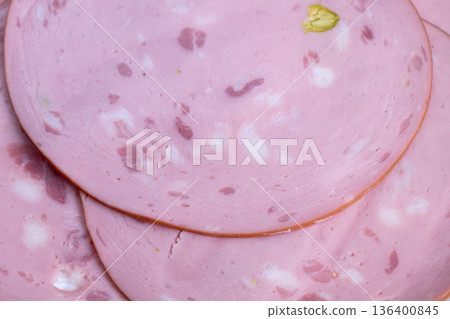 Freshly sliced mortadella with pistachio pieces on display, Universal supermarket presentation of mortadella showing decorative pistachio inclusions behind transparent glass 136400845