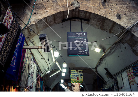 Jerusalem, Israel, December 13, 2025 Busy alleyways and atmospheric plays of light in the Christian Quarter souk of Jerusalem providing a glimpse of the variety of items displayed by local vendors. 136401164