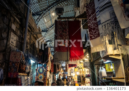 Jerusalem, Israel, December 13, 2025 Busy alleyways and atmospheric plays of light in the Christian Quarter souk of Jerusalem providing a glimpse of the variety of items displayed by local vendors. 136401173