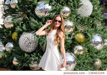 Woman in white dress posing near decorated christmas tree 136401544