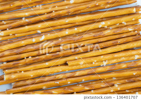 Casual snack during work break. Pretzel sticks resting on office workspace surface. Closeup of salted pretzel sticks placed on office desk for casual refreshment moments Casual snack during work break. Pretzel sticks resting on office workspace surface. Closeup of salted pretzel sticks placed on office desk for casual refreshment moments 136401707
