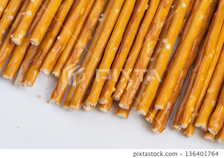 Closepacked crispy salted pretzels on white surface. Arrangement of crunchy salted pretzel sticks showing salt crystals and golden hue against minimal studio setting 136401764