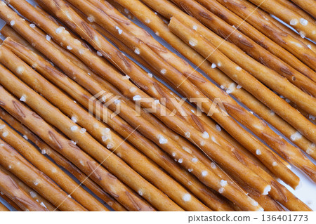 Diagonal salted pretzels presented neatly. Bright surface showcases salted pretzel sticks artistically. Elegant arrangement of pretzel rods with salt flakes on vivid backdrop 136401773