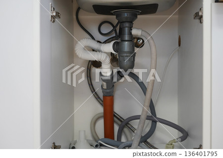 Under sink plumbing pipes and drainage system inside kitchen cabinet 136401795