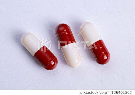 Three red and white loose capsules on clean surface, casual dosage layout for daily medication, scattered composition, bright studio lighting highlighting glossy shells and shadow 136401805
