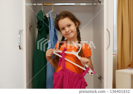 Smiling little child girl choosing colorful dress from wardrobe at home Smiling little child girl choosing colorful dress from wardrobe at home 136401832