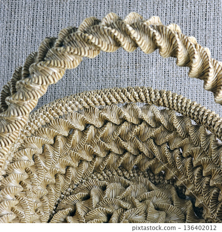 A woven straw basket against burlap background. Close-up. Details. Eco-friendly. Handmade basket for interior decoration and use as container for collecting fruits, vegetables, and mushrooms. 136402012