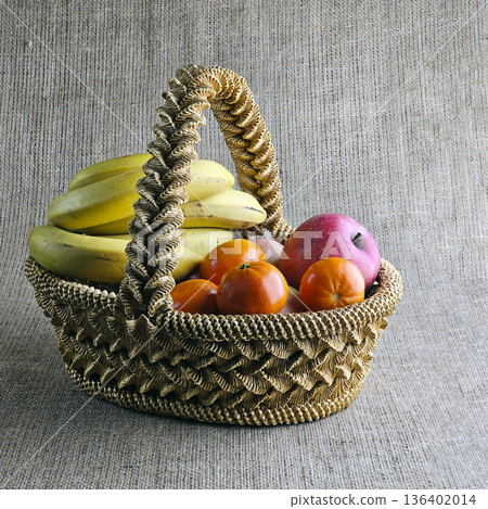 A woven straw basket against a burlap background. Close-up. Eco-friendly. The handmade basket is filled with fruit 136402014