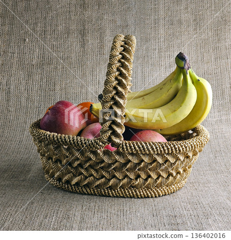 A woven straw basket against a burlap background. Close-up. Eco-friendly. Handmade basket is filled with fruit A woven straw basket against a burlap background. Close-up. Eco-friendly. Handmade basket is filled with fruit 136402016