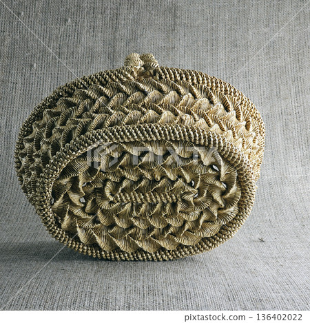 Woven straw basket against burlap background. Close-up. Eco-friendly. Handmade basket for interior decoration and use as a container for collecting fruits, vegetables, and mushrooms. 136402022