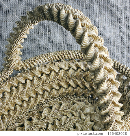 Woven straw basket against burlap background. Close-up. Details. Eco-friendly. Handmade basket for interior decoration and use as a container for collecting fruits, vegetables, and mushrooms. Woven straw basket against burlap background. Close-up. Details. Eco-friendly. Handmade basket for interior decoration and use as a container for collecting fruits, vegetables, and mushrooms. 136402028