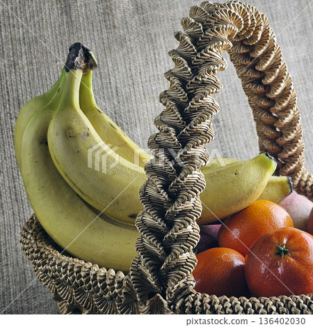 Woven straw basket on a burlap background. Close-up. Details. Eco-friendly. The handmade basket is filled with fruit Woven straw basket on a burlap background. Close-up. Details. Eco-friendly. The handmade basket is filled with fruit 136402030
