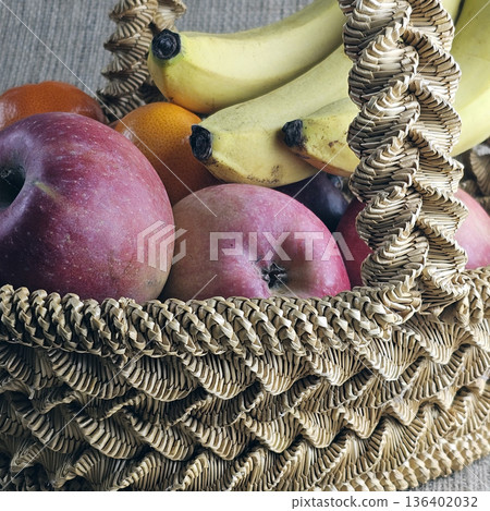 A woven straw basket on a burlap background. Close-up. Details. Eco-friendly. Handmade basket is filled with fruit A woven straw basket on a burlap background. Close-up. Details. Eco-friendly. Handmade basket is filled with fruit 136402032