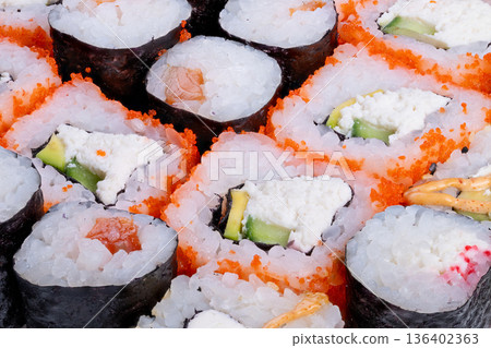 Vibrant sushi assortment for sharing. Colorful sushi rolls displayed for joyful gathering. Fresh sushi selections complemented by roe in lively communal dining setting 136402363