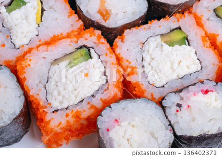 Assorted sushi rolls for sharing, uramaki and maki varieties with sesame and crab accents, lively casual party atmosphere, ideal for catering, events, and social food scenes 136402371