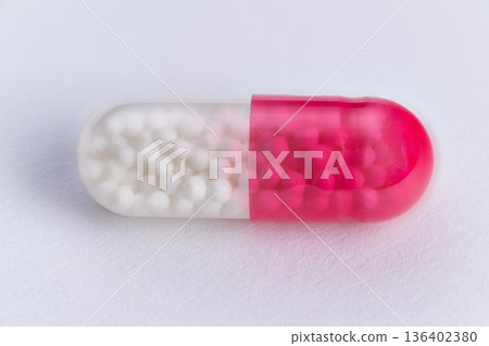 Macro shot of transparent pill with pink and white contents on white background. Detailed studio photograph of capsule with visible granules and sterile minimalist setting Macro shot of transparent pill with pink and white contents on white background. Detailed studio photograph of capsule with visible granules and sterile minimalist setting 136402380