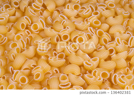 Closeup of textured dry pasta shells. Detailed view of warmhued uncooked pasta shapes. Sharp focus on rustic dry pasta with distinct ridges and warm color tones 136402381