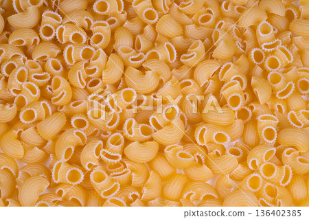 Closeup of dry pasta shells. Detailed shot of golden dry pasta shells with ridges. Dramatic macro photograph capturing textured dry pasta shells in warm tones for visuals Closeup of dry pasta shells. Detailed shot of golden dry pasta shells with ridges. Dramatic macro photograph capturing textured dry pasta shells in warm tones for visuals 136402385