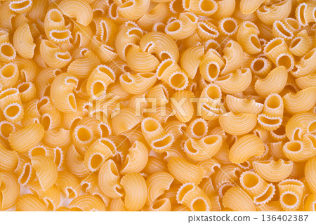 Uniform macaroni shapes showcased under specialized industrial lighting. Production line for ridged pasta with distinct surface qualities and branding applications 136402387