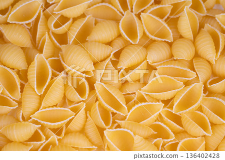 Conchiglie pasta forms create inviting kitchen atmosphere. Closeup of dried pasta shells arranged to showcase ridges and curled forms under warm golden lighting Conchiglie pasta forms create inviting kitchen atmosphere. Closeup of dried pasta shells arranged to showcase ridges and curled forms under warm golden lighting 136402428