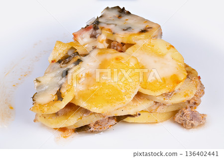 Styled potato slice on white plate, layered rounds topped with melted cheese and herb bits, angled composition for social feed with visible texture and appetizing edge browning 136402441