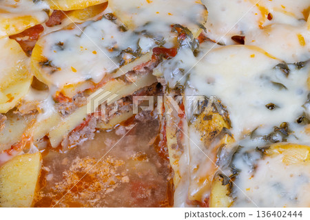 Layered potato dish with melted cheese. Golden potato slices topped with bubbling cheese and herbs. Melted cheese over layered thin potato slices with herbs and sauce Layered potato dish with melted cheese. Golden potato slices topped with bubbling cheese and herbs. Melted cheese over layered thin potato slices with herbs and sauce 136402444