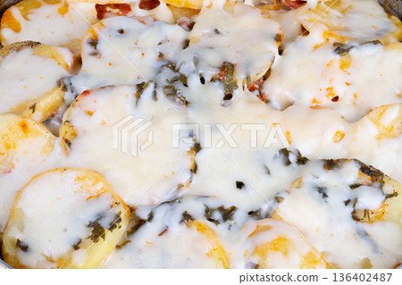 Oven roasted potato rounds topped with melted cheese and basil leaves. Mouthwatering baked potato slices generously layered with cheese and fragrant basil leaves for flavor 136402487