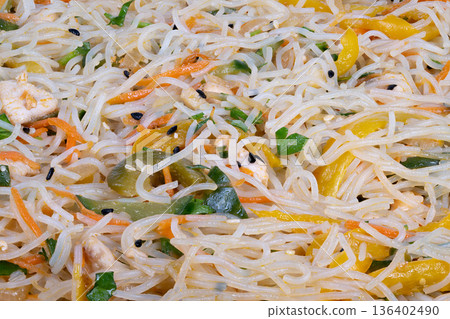 Detailed noodle image. Closeup of noodles with herbs. Macro photograph highlighting rice noodles and herbs. Intricate macro shot capturing noodle texture and scattered herbs 136402490