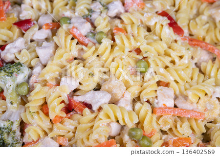 Creamy fusilli pasta with vegetables, tossed in parmesan dressing, diced chicken, peas and julienned red pepper, warm cozy kitchen vibe, prepared by home cook for family meal Creamy fusilli pasta with vegetables, tossed in parmesan dressing, diced chicken, peas and julienned red pepper, warm cozy kitchen vibe, prepared by home cook for family meal 136402569