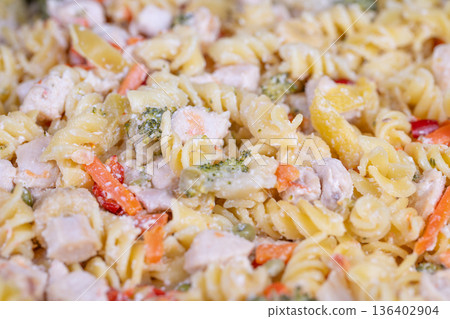Detailed view of spiral pasta coated with dressing and colorful vegetables. Vivid image showcasing creamy rotini with peas carrots corn and chicken in fine detail 136402904