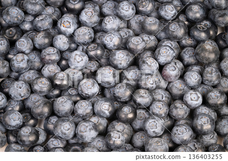 Dusty blue blueberries arranged in heap. Natural varied frozen blueberries with textured skins. Closeup of frozen blueberries showcasing rustic farm harvest and textured skins 136403255