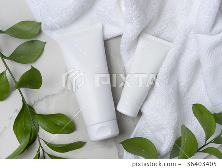 Mockup of blank white cream tubes near white bath towel and green leaves. Unbranded cosmetic 136403405
