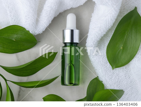 Glass dropper bottle near white bath towel and green leaves, skincare serum packaging mockup 136403406