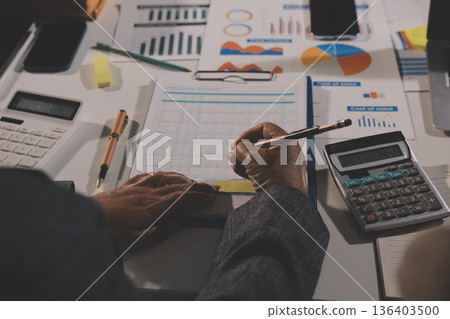 business documents on office table with tablet, smart phone and laptop and two colleagues discussing data business documents on office table with tablet, smart phone and laptop and two colleagues discussing data 136403500