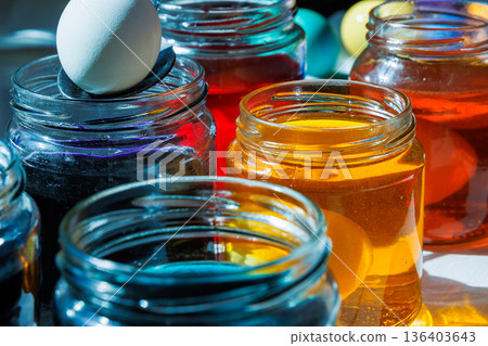 Close up of a hand using a spoon to dip a white egg into a glass jar with colorful easter dye Close up of a hand using a spoon to dip a white egg into a glass jar with colorful easter dye 136403643