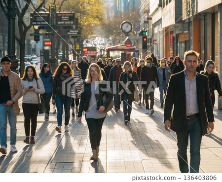 Crowded street scene with people walking in a busy urban area during daytime with sunlight and shadows 136403806